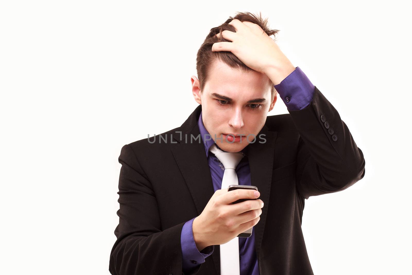 Young businessman amazedly
looking at the phone holding on to the head isolated on white