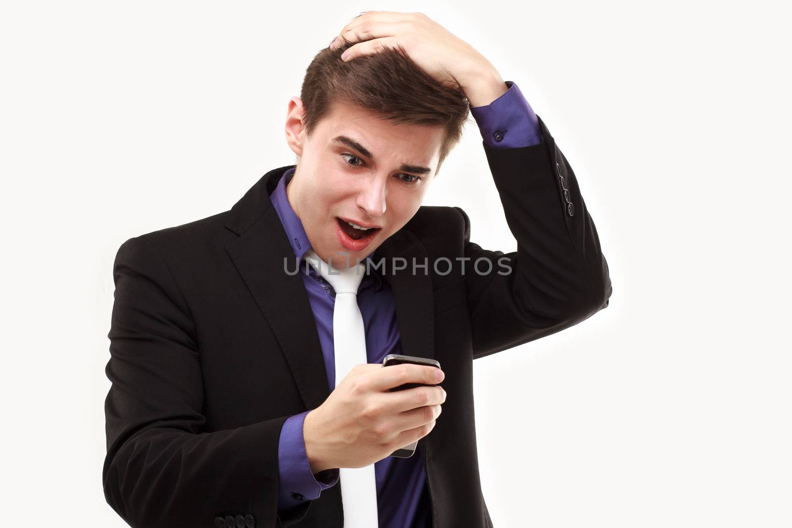 Young businessman amazedly
looking at the phone holding on to the head isolated on white