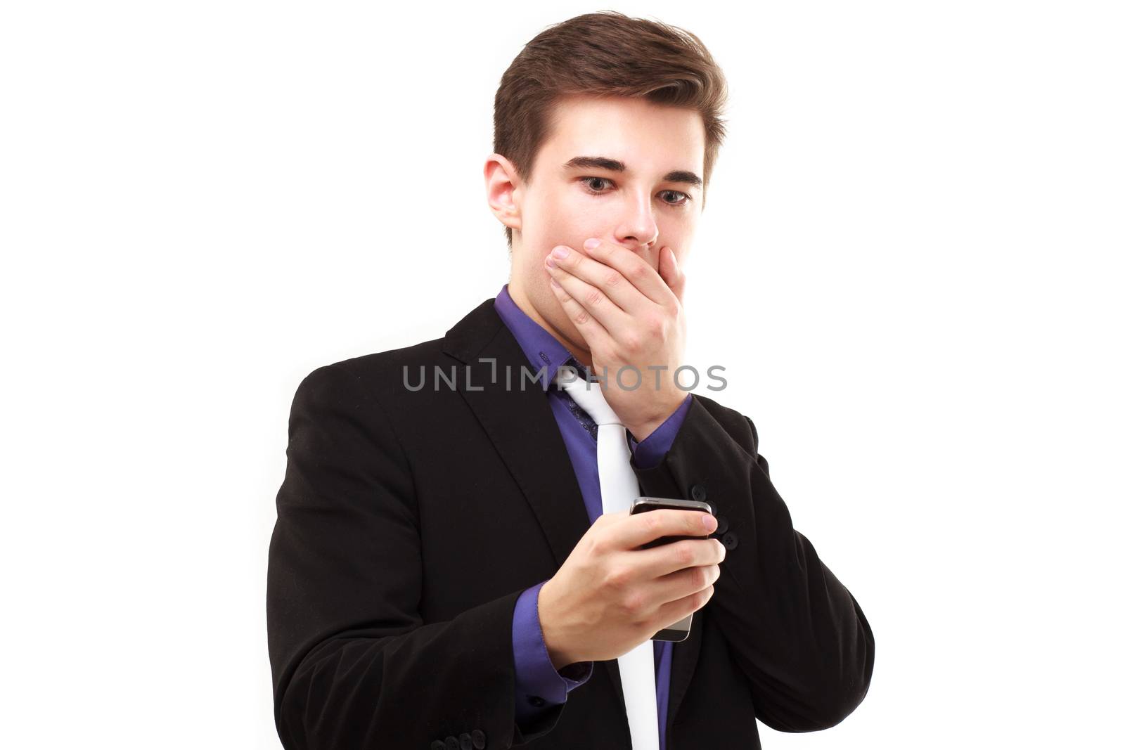 Young businessman fearfully looking at the phone and covers his mouth isolated on white