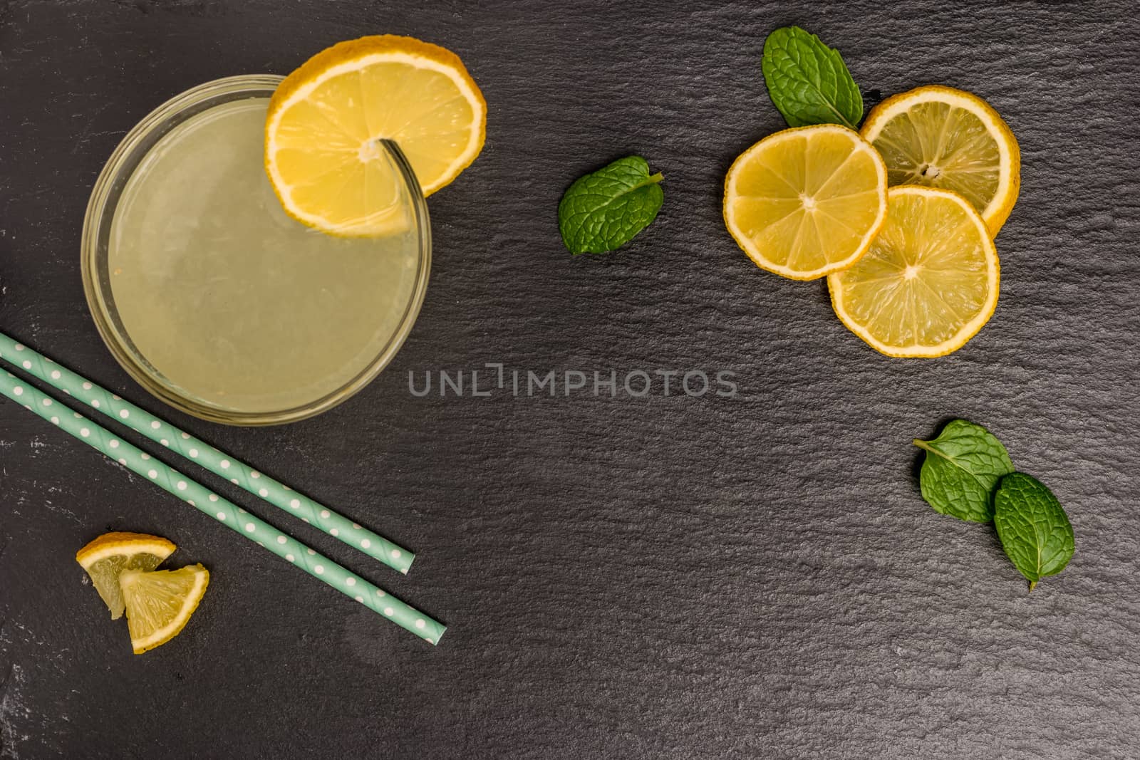 Glass of homemade lemonade with mint and lemon wedges on slate. Top view with copy space.