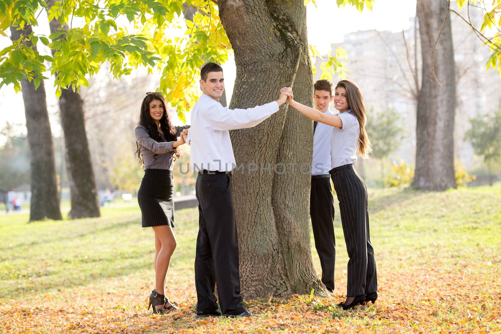 Group of young business people standing in a park hugging a tree trunk.