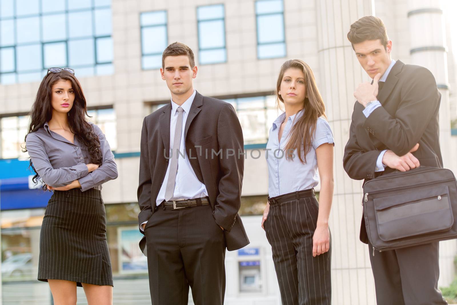 Group of young successful business people standing in front of office building dressed in suits. With a serious expression on their faces looking at the camera.