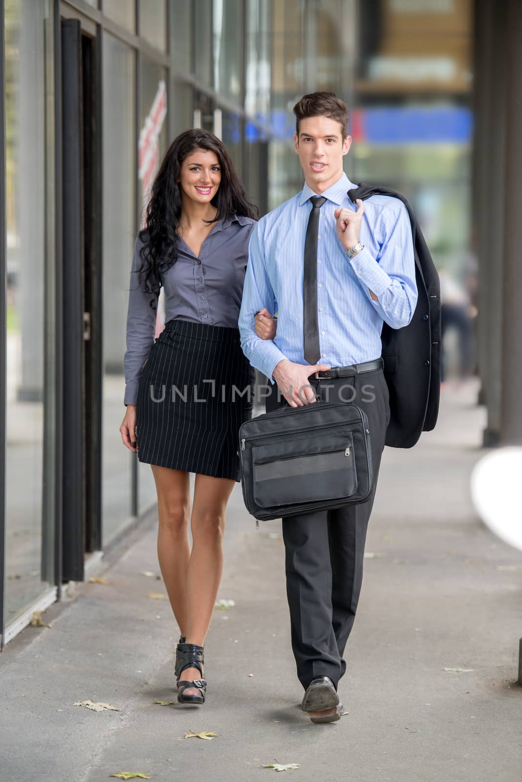 Handsome pair of young businessmen and businesswomen walking outside. Looking at camera.