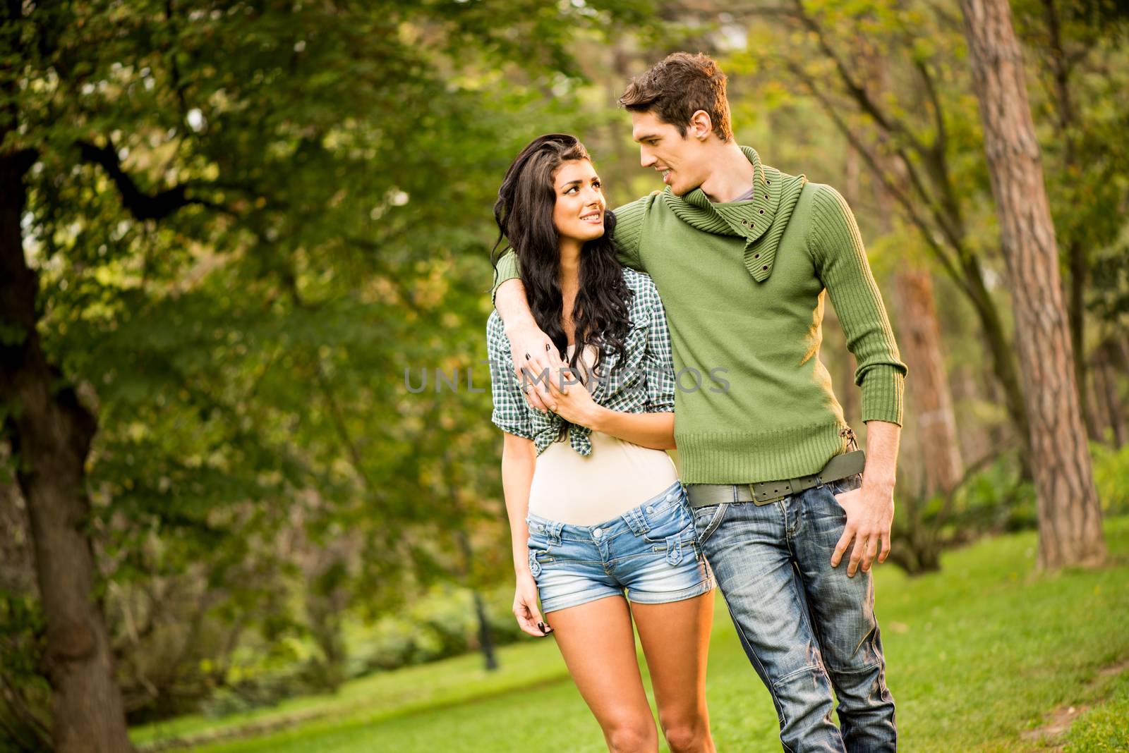 Young cheerful couple embracing and smiling walking through the park.