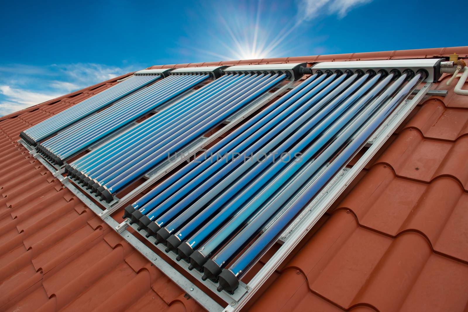 Vacuum collectors- solar water heating system on red roof of the house.