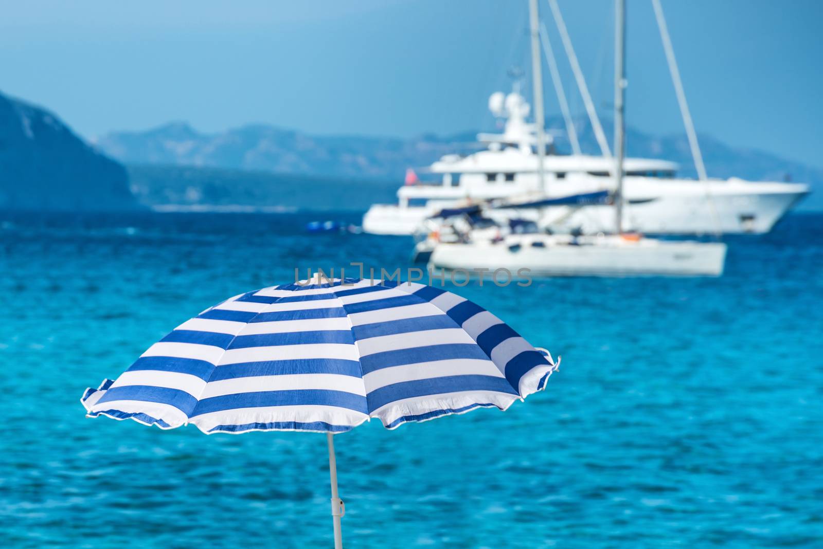 Colorful umbrellas on the tropical beach with blue sea and yachts as background