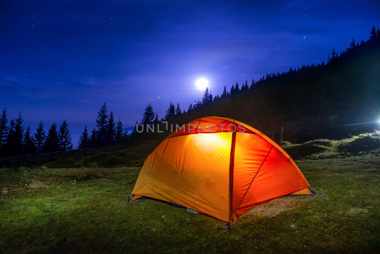 Illuminated orange camping tent under moon, stars at night