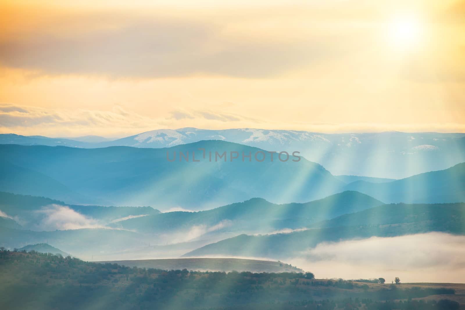 Blue mountains covered with mist against sunset. Bright sun shining on the sky