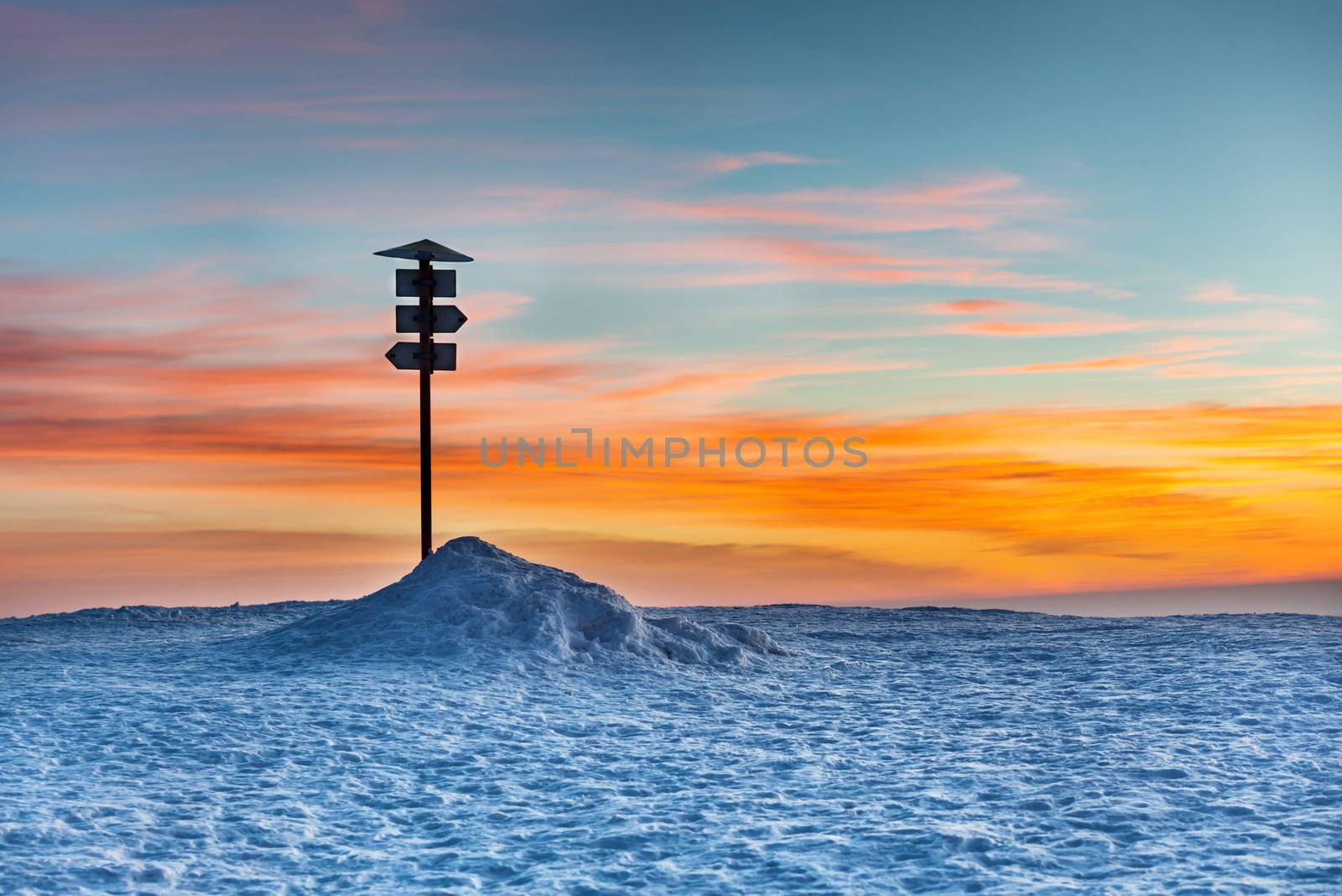 Direction sign on the top of winter mountain against sunset