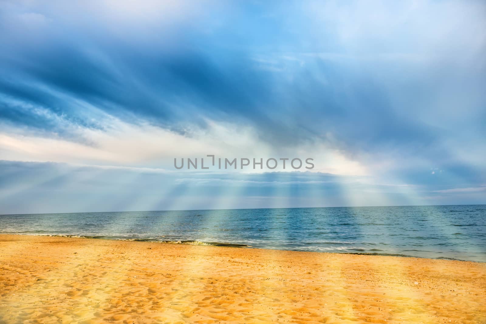 Sun shining through clouds with sunbeams above tropical beach with yellow sand and blue sea