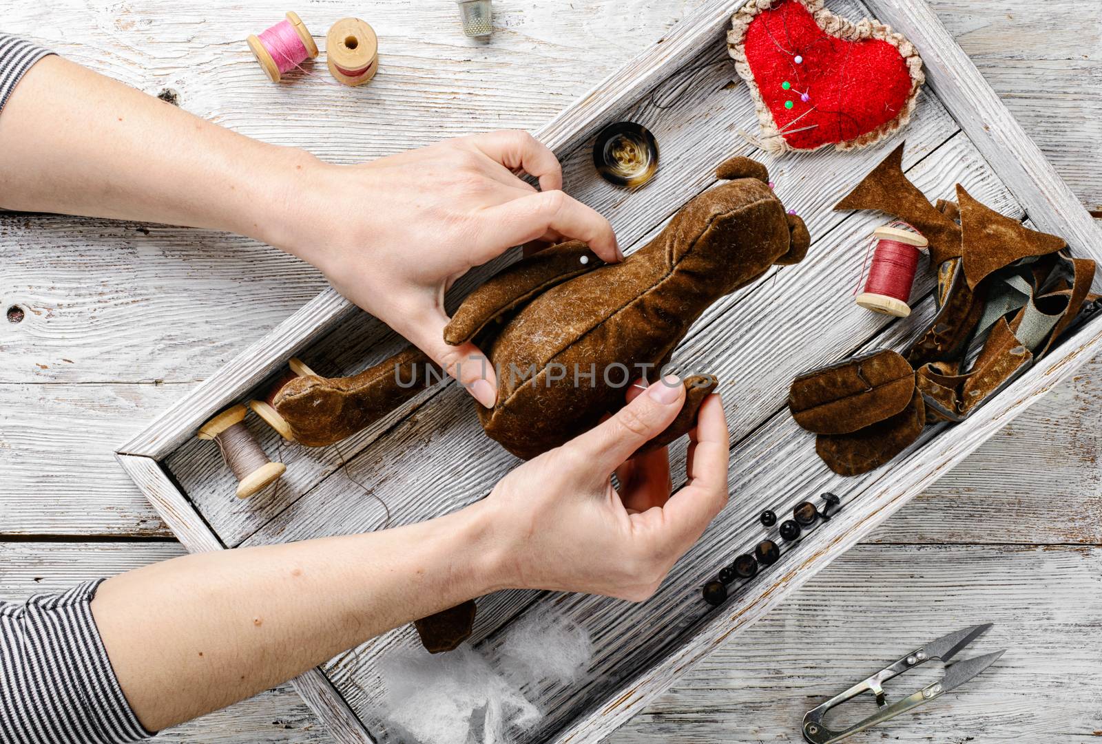 Women's hands in the process of manufacturing soft bear toys and sewing tools