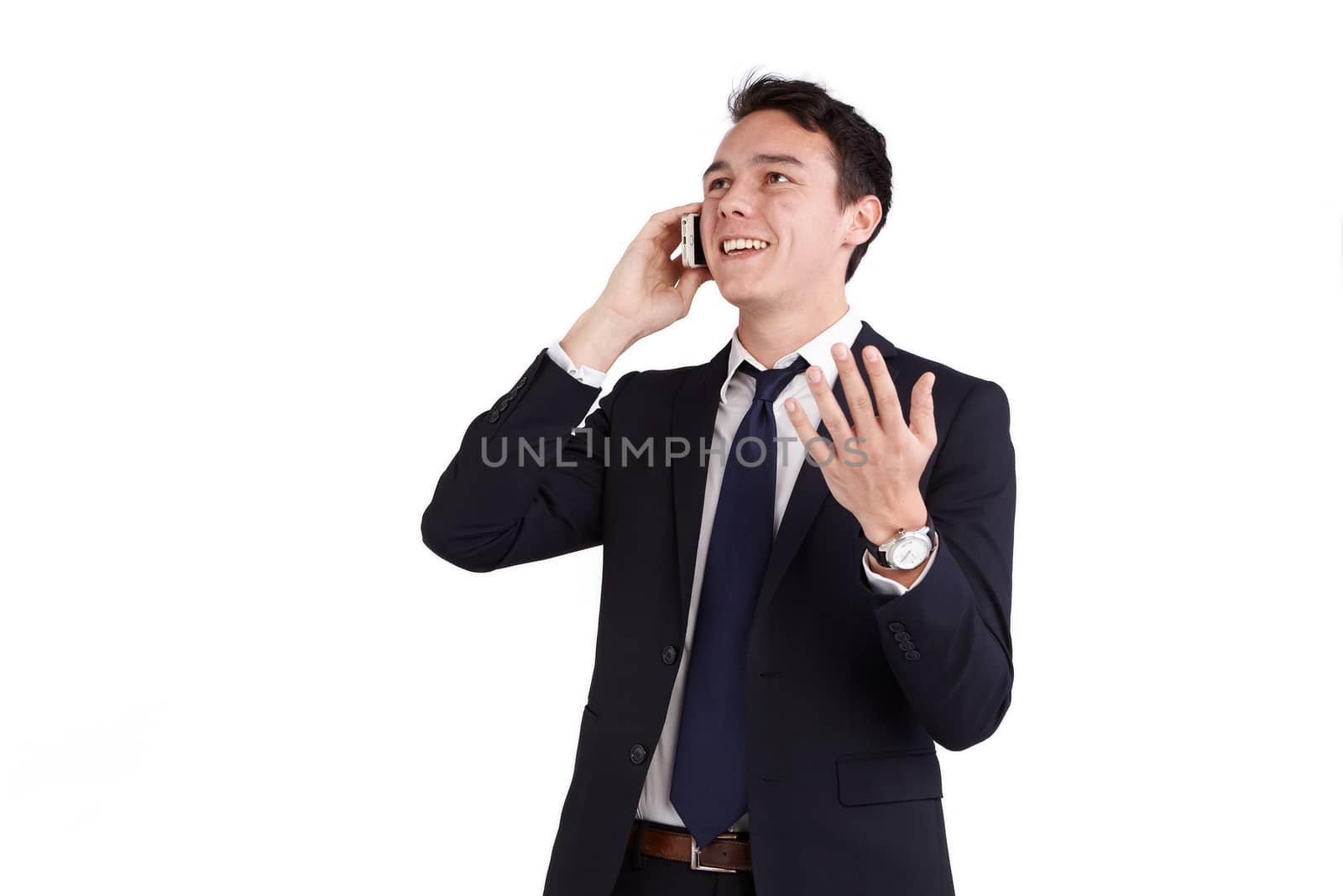 A young caucasian male businessman smiling holding a mobile phone while raising his hand looking away from camera.