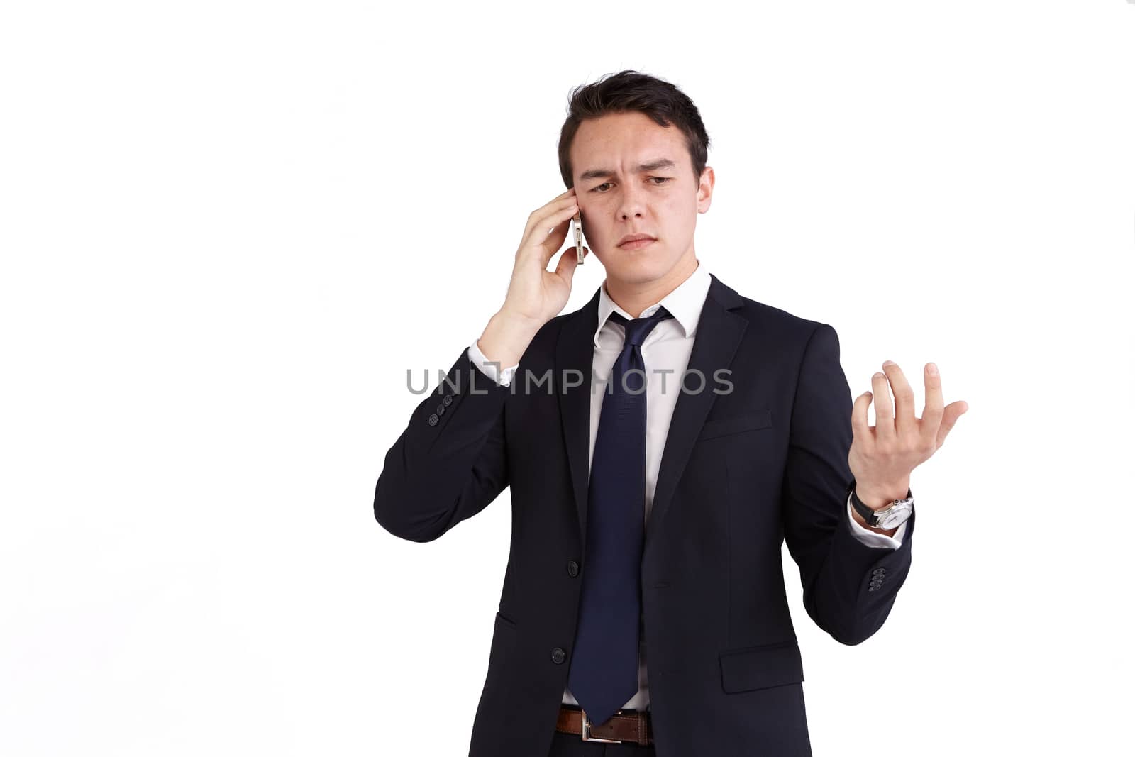 A young caucasian male businessman frowns with raised hand while holding a mobile phone looking away from camera.