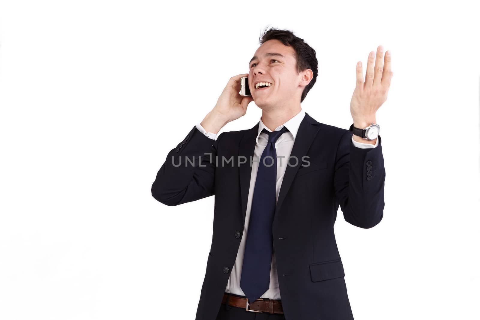 A young caucasian male businessman smiling with raised hand holding a mobile phone looking away from camera.