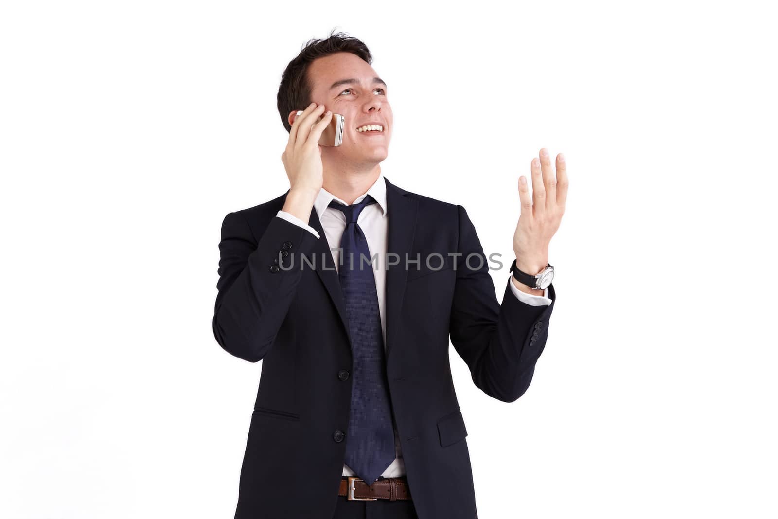 A young caucasian male businessman smiling with raised hand holding a mobile phone looking away from camera.