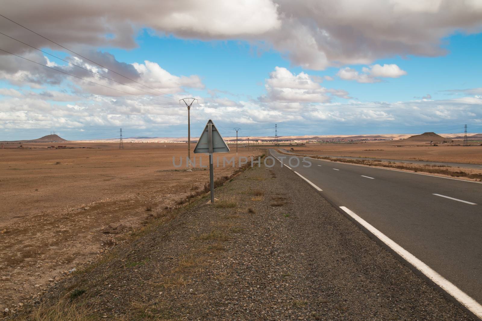 New road cross the country in Morocco,between Marrakesh and Essaouira. Autumn fields with a light color of the dry soil are lining the road. Cloudy sky.