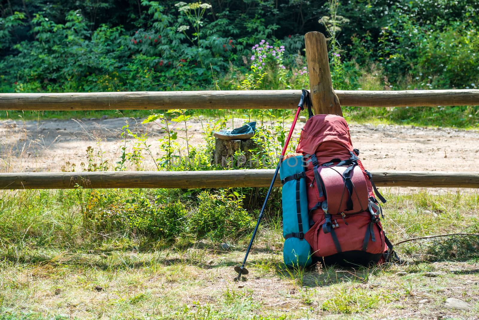 Backpack and trekking pole standing near fence at green grass countryside. Travel outdoor background