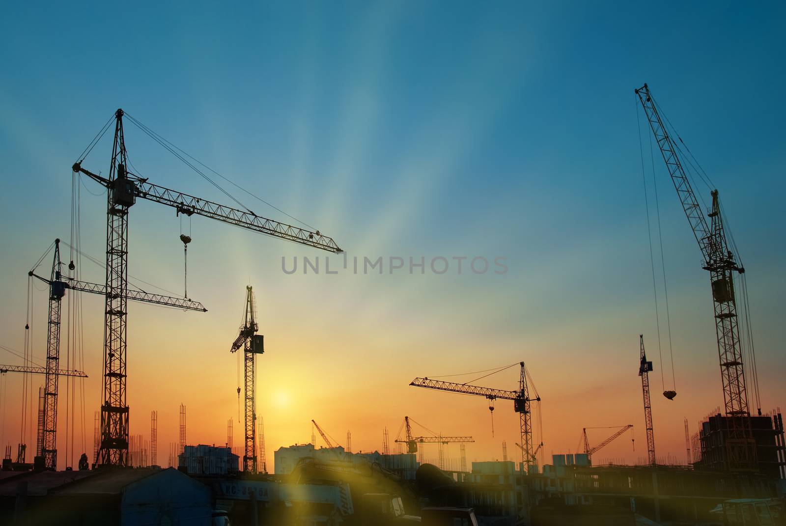 Industrial landscape with silhouettes of cranes over sunset