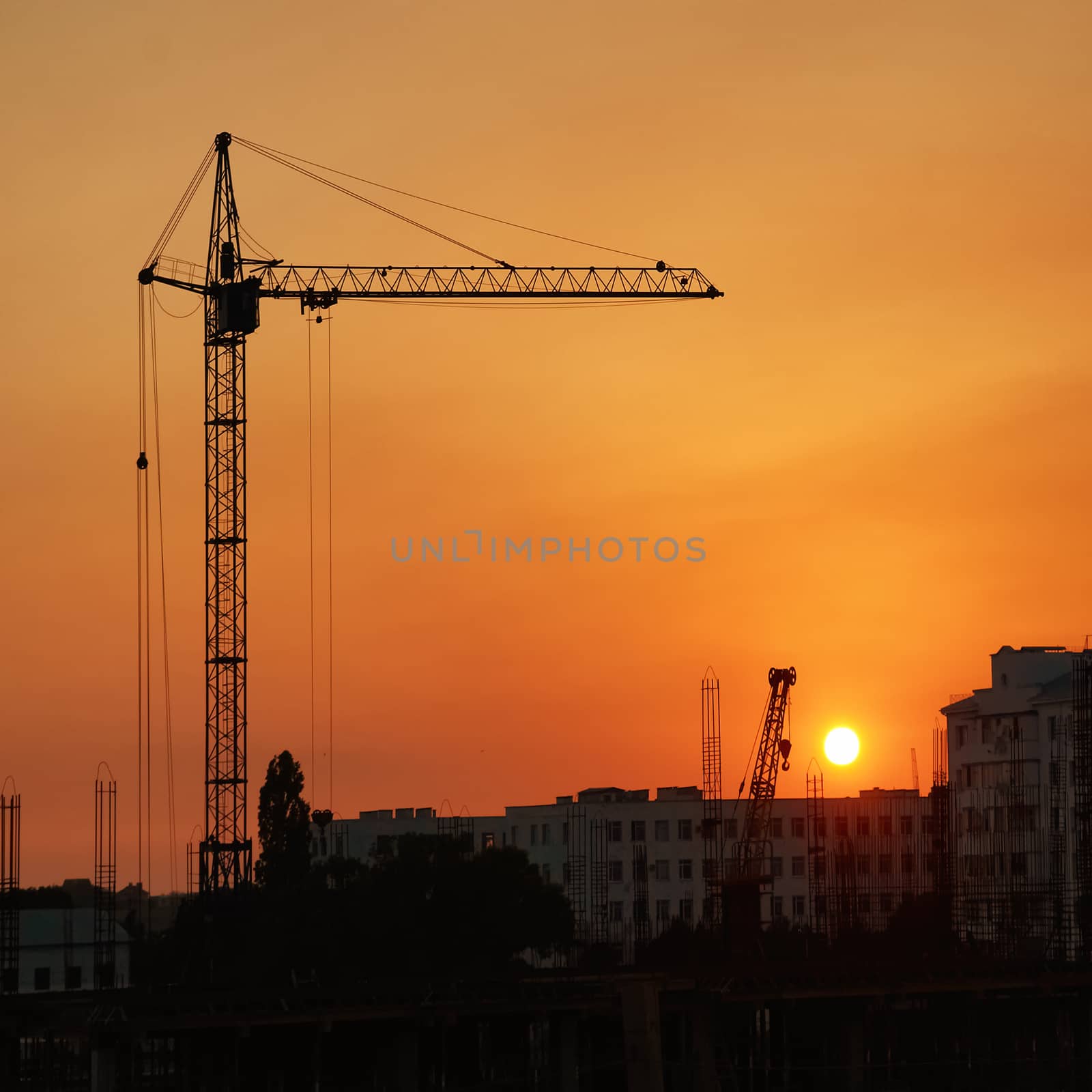 Industrial cranes over orange sunset with red sun