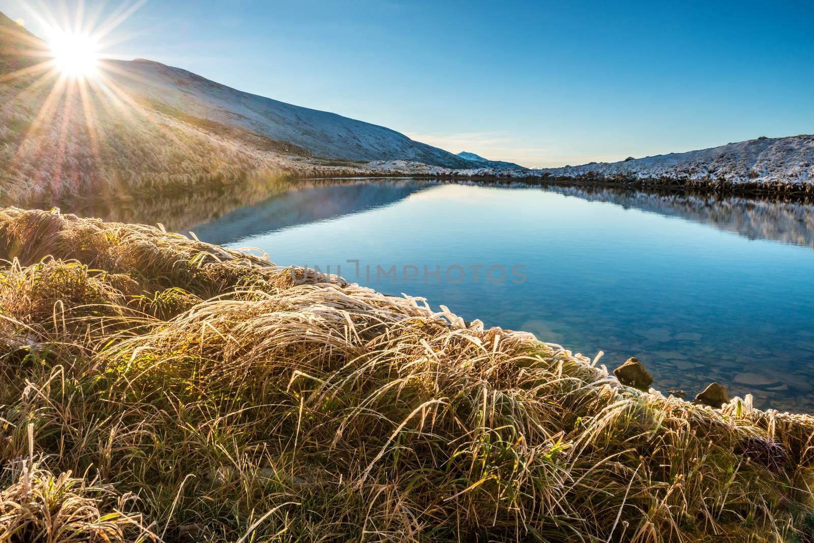 Mountain lake with blue water and sunset over it. Shining sun above the bank