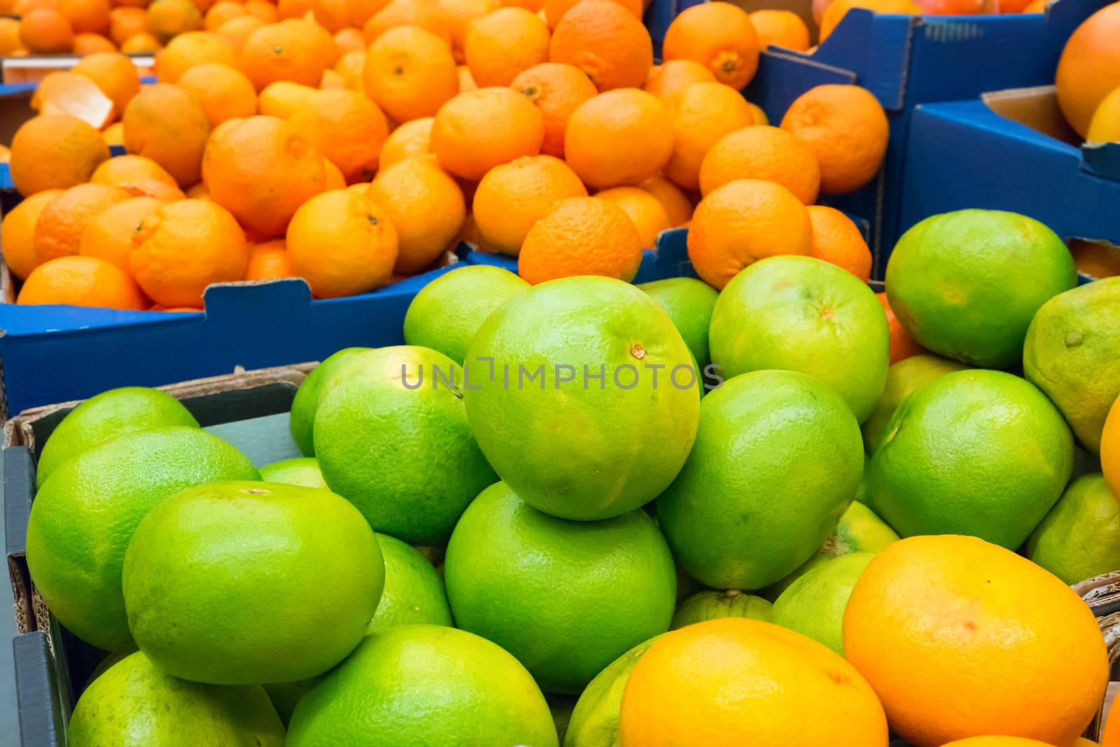 Pile of fresh green pamelos and oranges in the crates at market