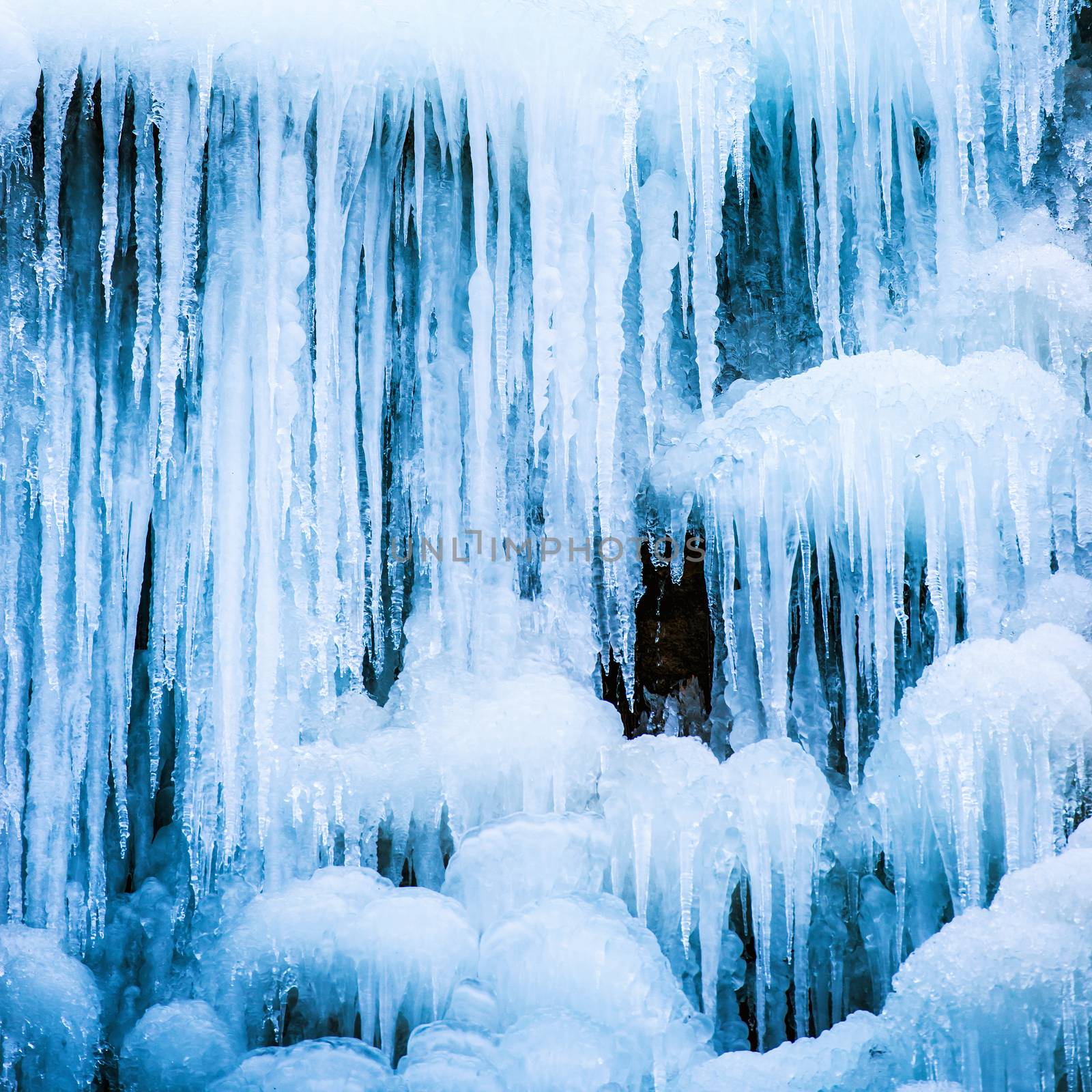 Frozen ice waterfall of blue icicles on the rock