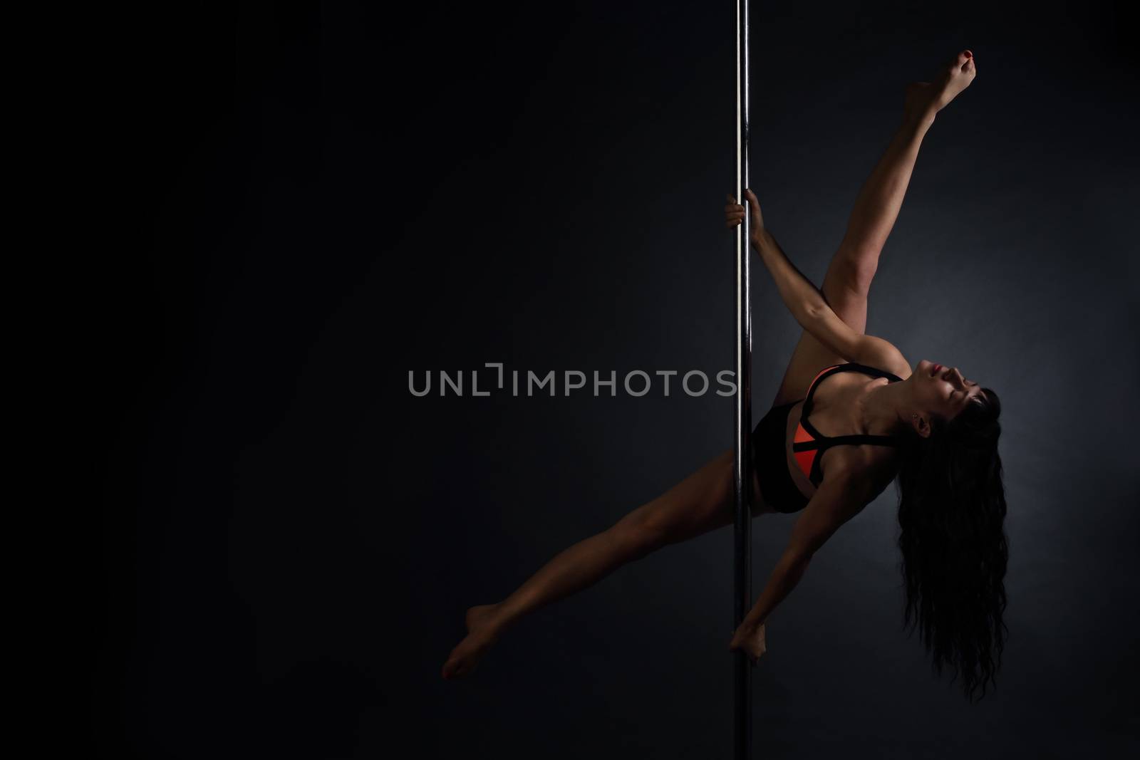 Beautiful slim woman performing pole dance on dark background
