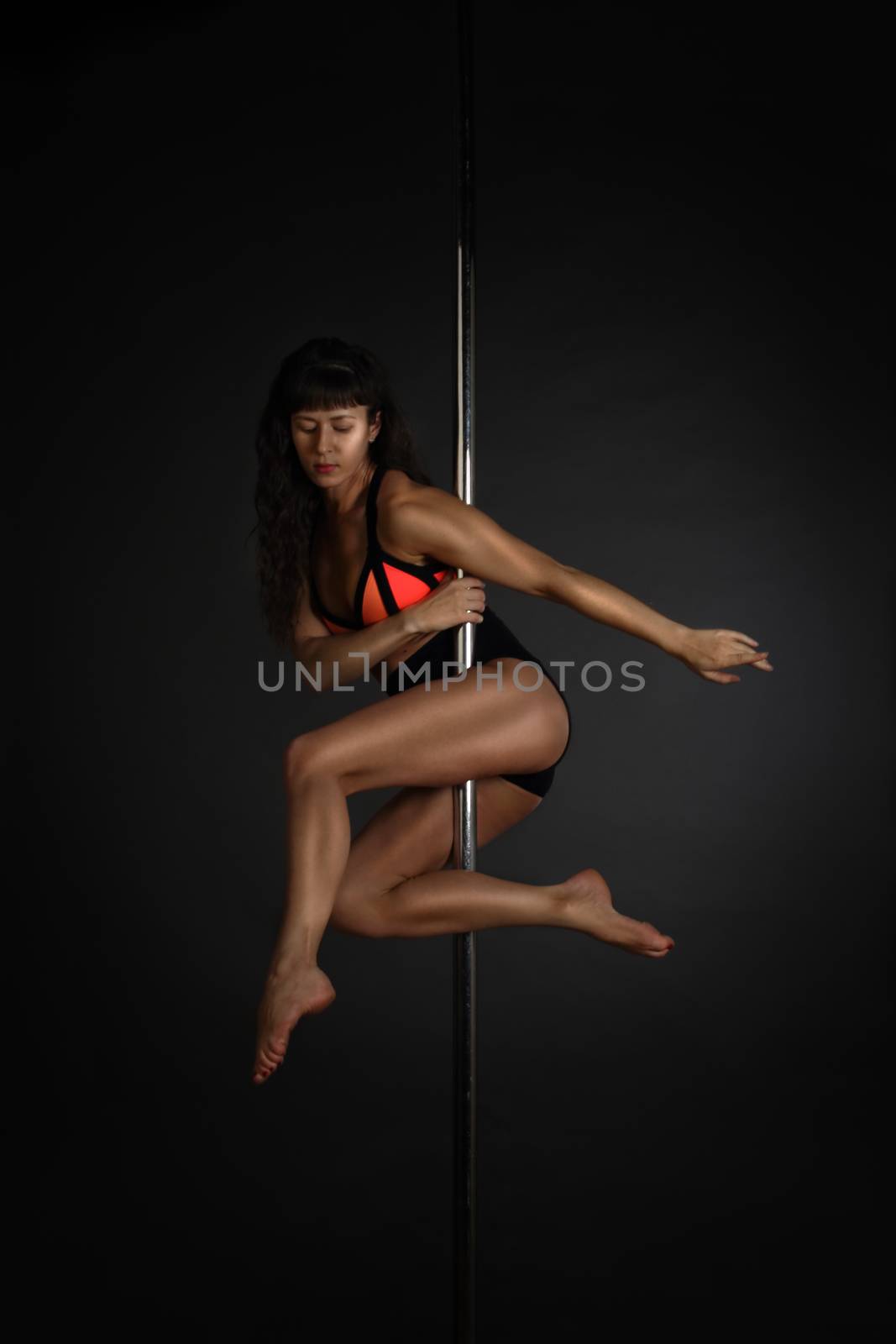 Beautiful slim woman performing pole dance on dark background