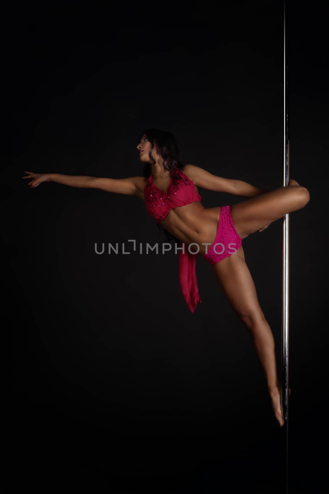 Beautiful woman performing pole dance on dark background