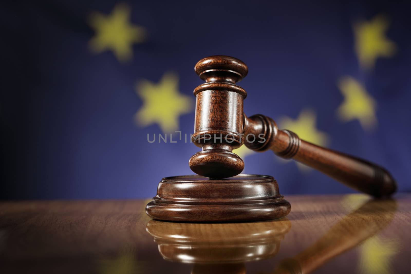 Mahogany wooden gavel on glossy wooden table. Flag of European Union, EU,  in the background.