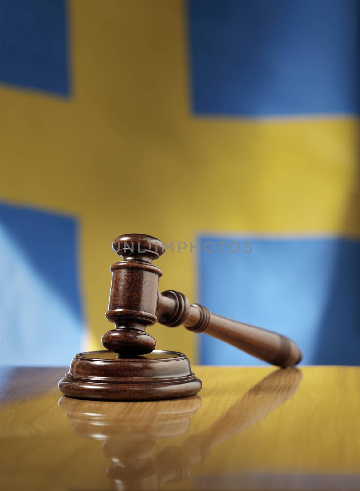 Mahogany wooden gavel on glossy wooden table, flag of Sweden in the background.