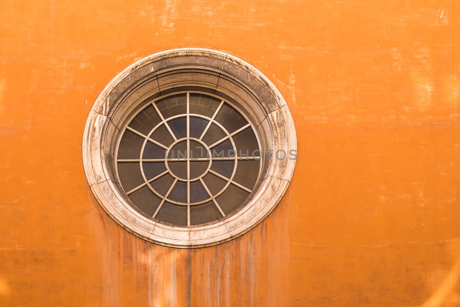 Typical orange color of the facade of a house in Rome. Unusual round window, made of segments.