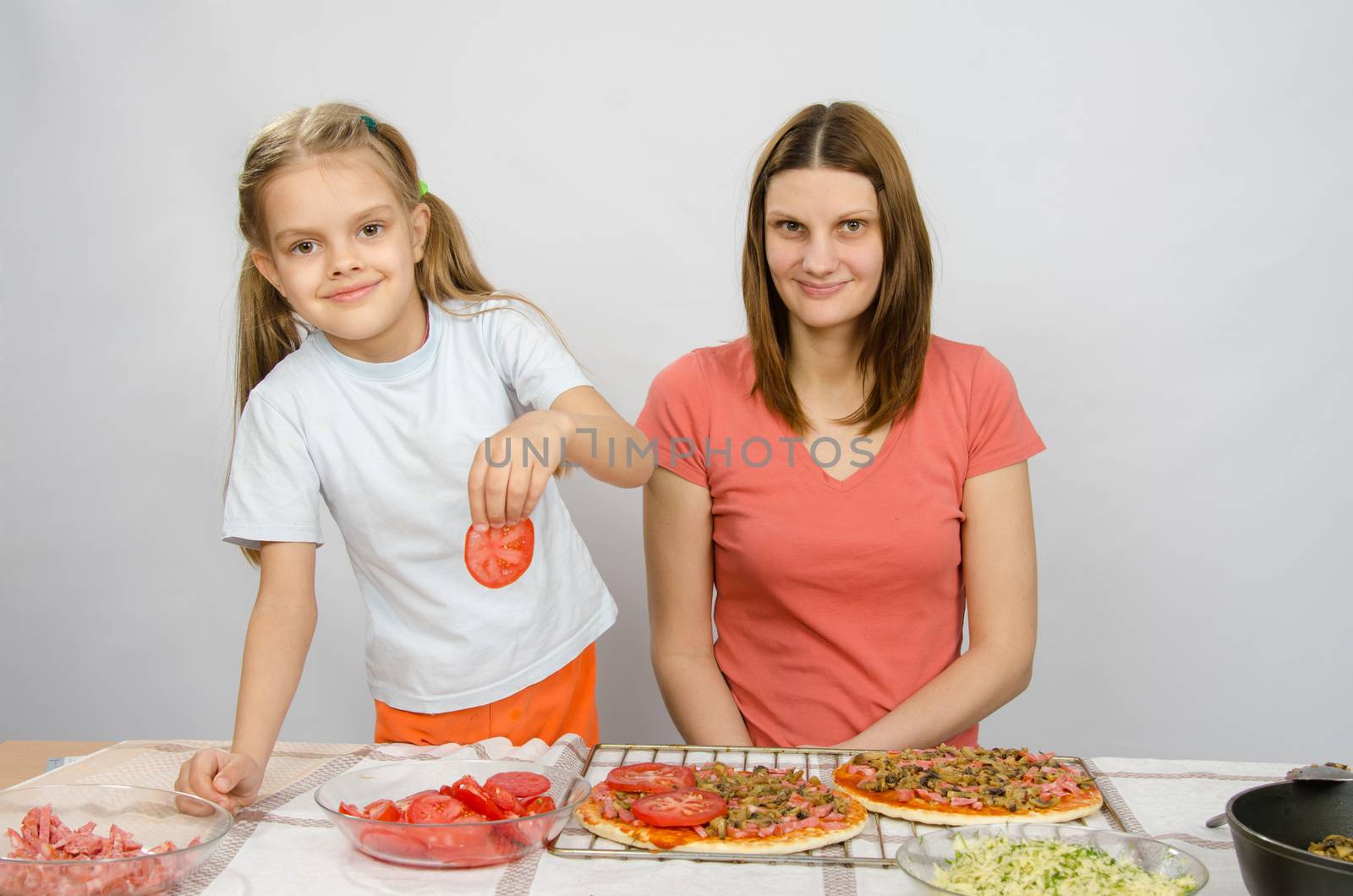 Six-year girl puts on the pizza tomatoes under the supervision of mum