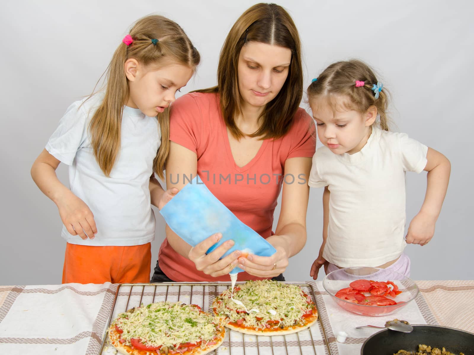 Two little girls are watching with interest as the mother is watering mayonnaise pizza by Madhourse