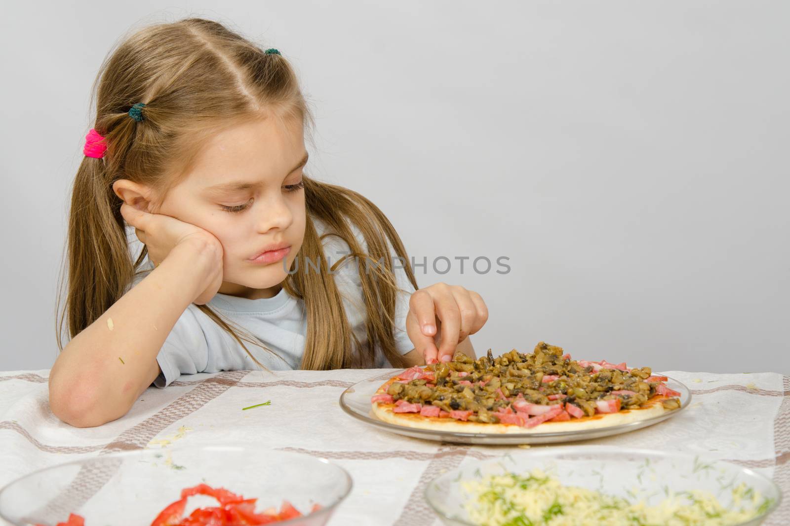 Little six year old girl sitting at the table and picks unfinished pizza by Madhourse
