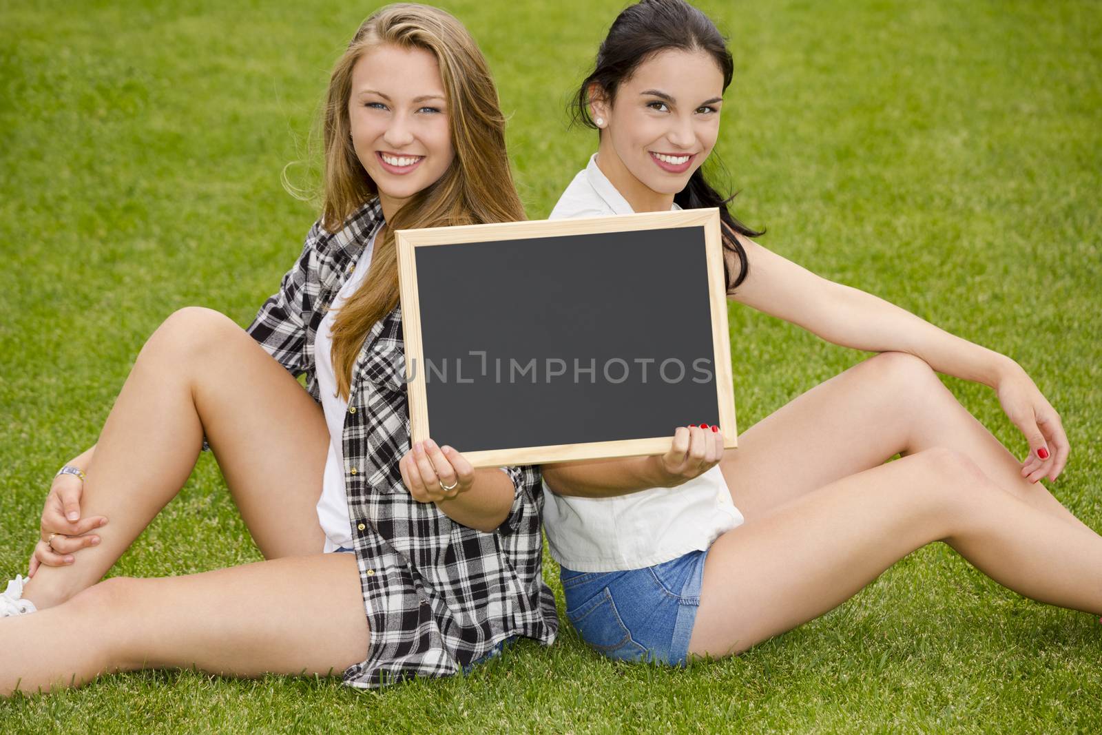 Tennage students sitting on the grass and holding a chalkboard