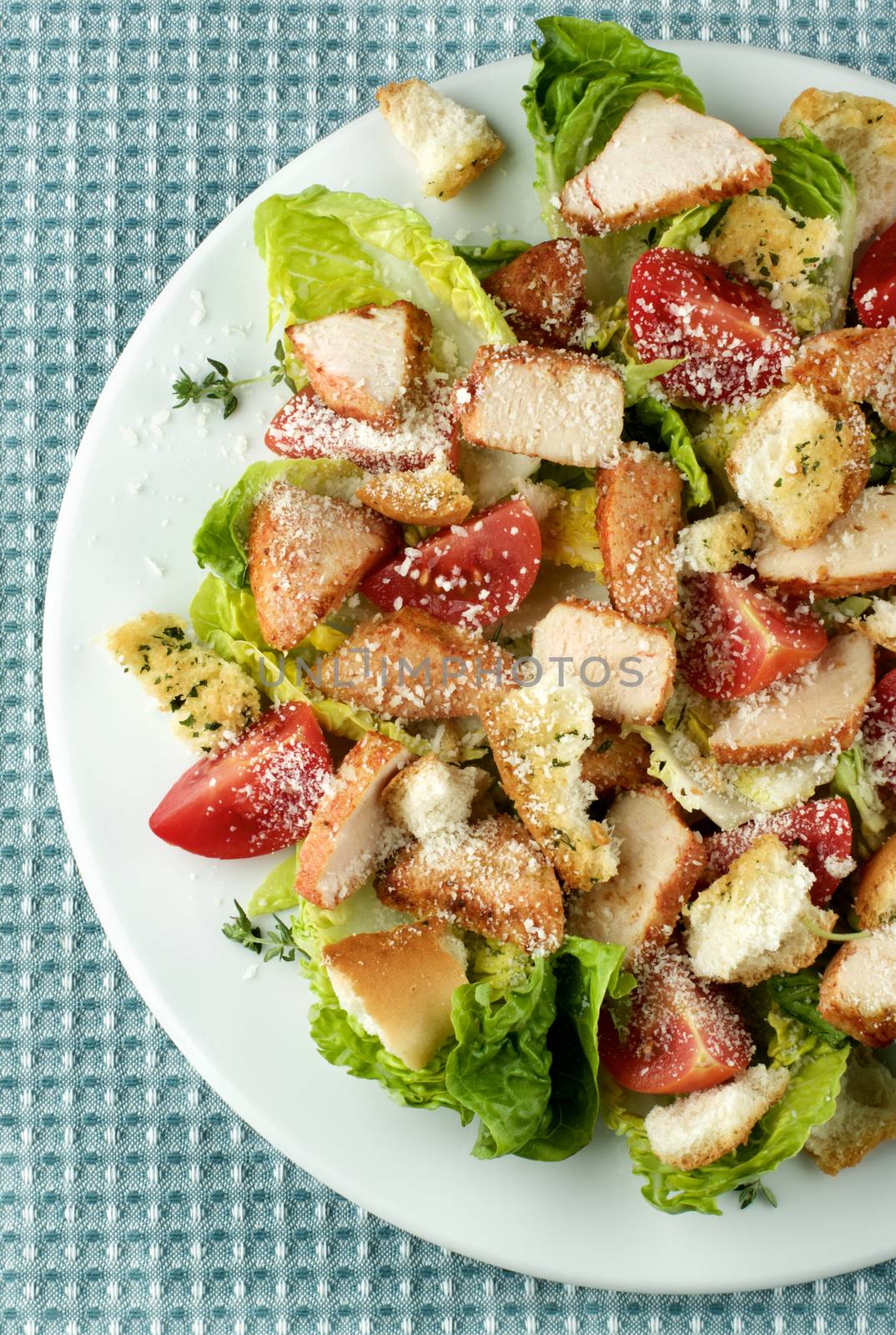Delicious Caesar Salad with Roasted Chicken Breast, Garlic Crouton, Romaine Lettuce, Cherry Tomatoes and Grated Parmesan Cheese closeup on White Plate. Top View on Napkin