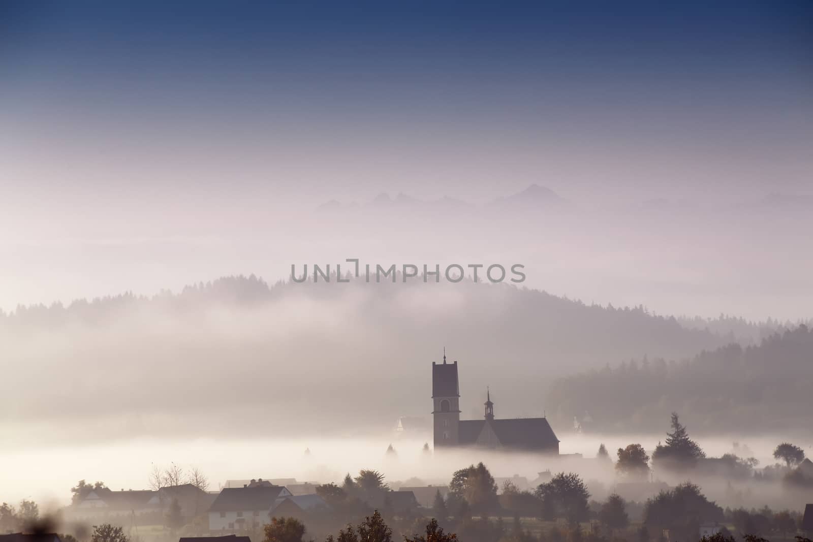 Foggy morning in small town. Church in a mist. Poland (malopolska) autumn sunny morning.