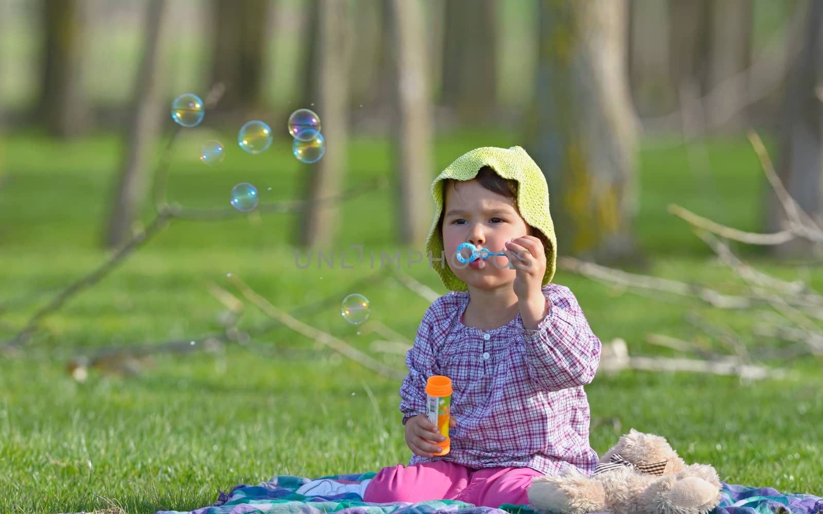 little girl is blowing a soap bubbles in forest