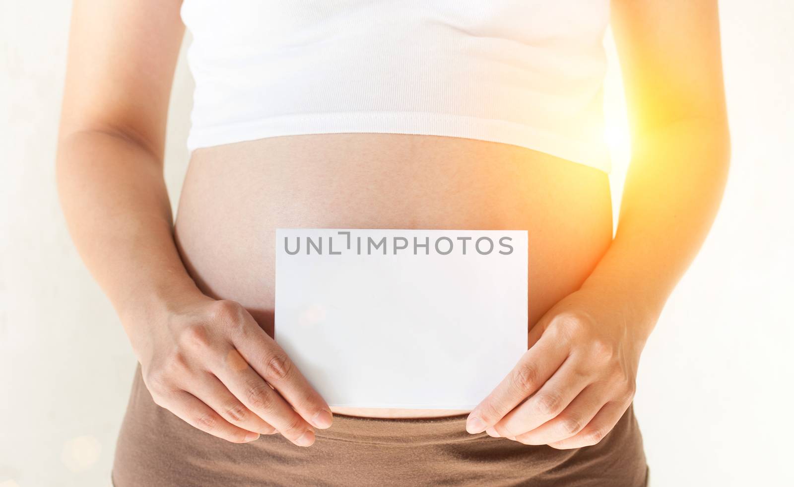 Pregnant woman holding her hands on the belly and holding a blank white paper mockup