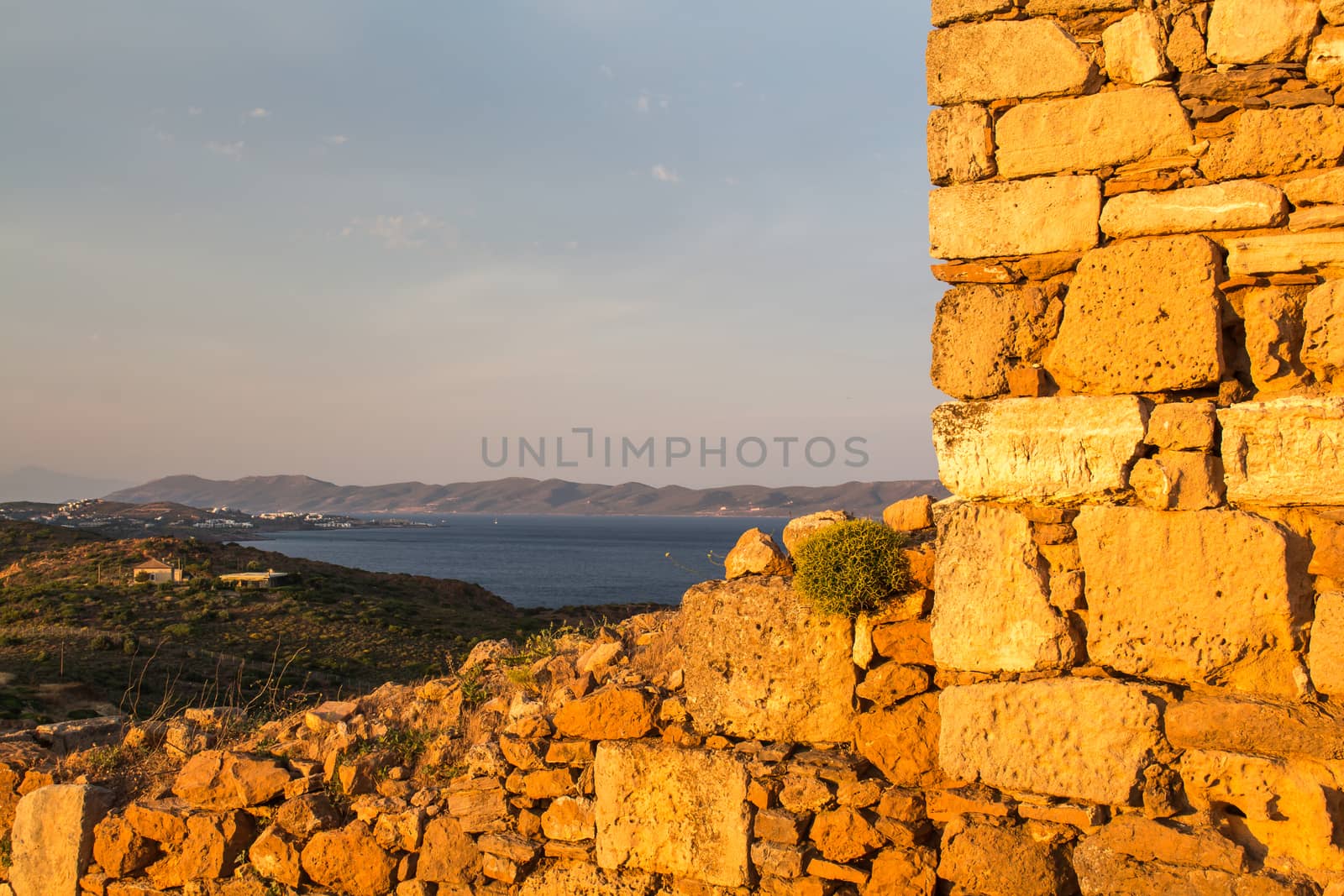 Golden color of the stone wall during the sunset. Mountains and sea with an evening sky in the background. Cape Sounion, Greece.