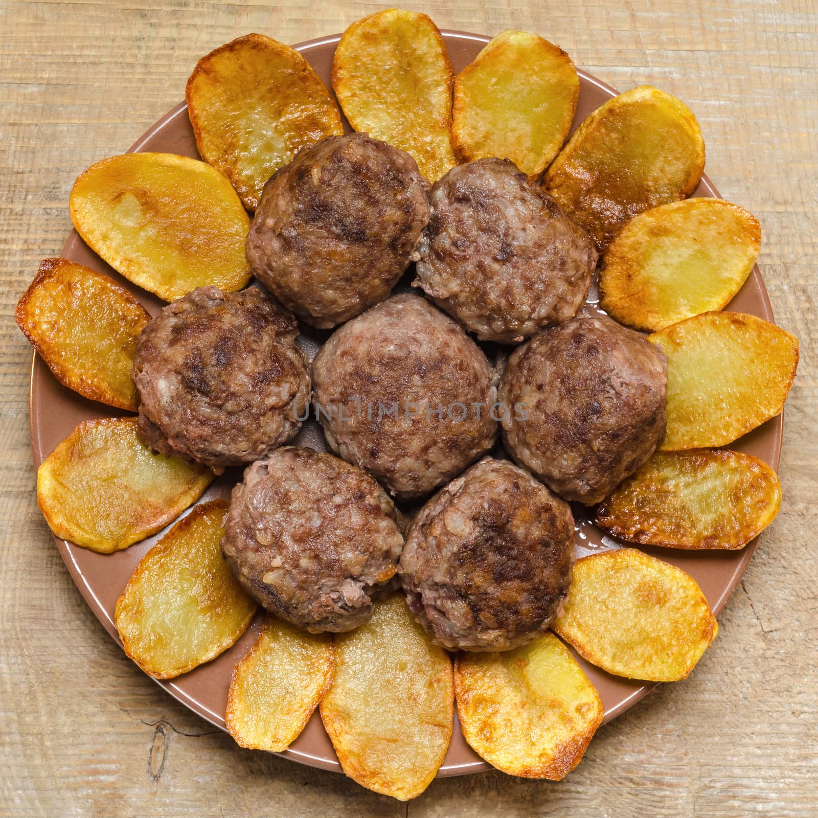 Fried meatballs with rice and French fries on the plate on wooden background.