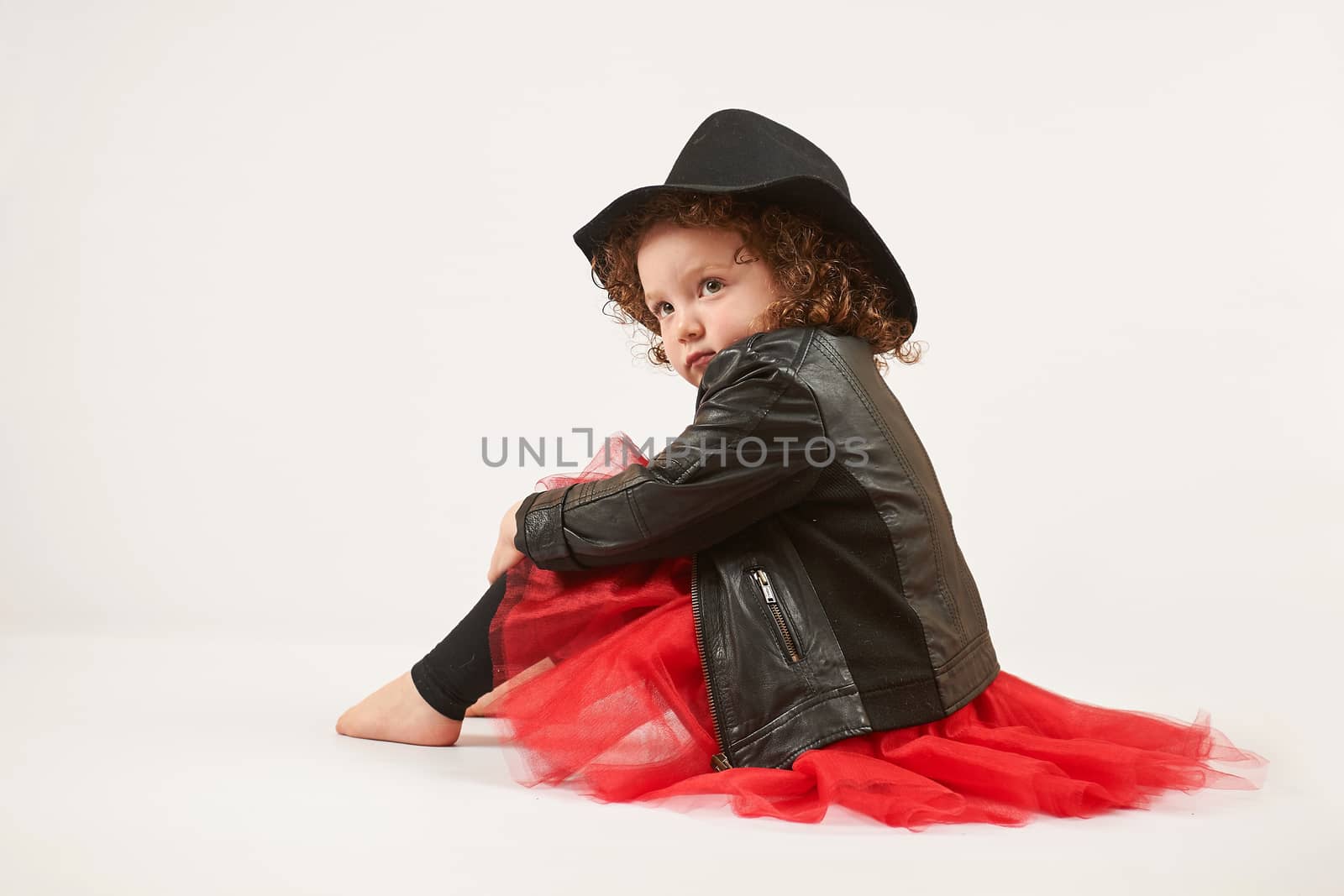 Little girl with black hat sitting and pouting. side view