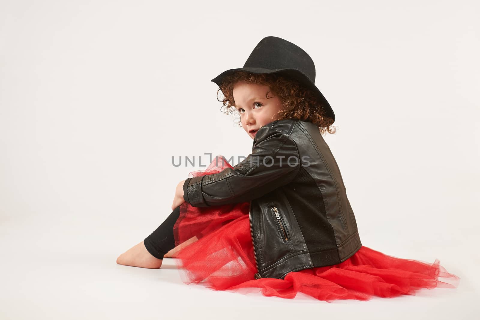 Little girl with black hat sitting and pouting. side view