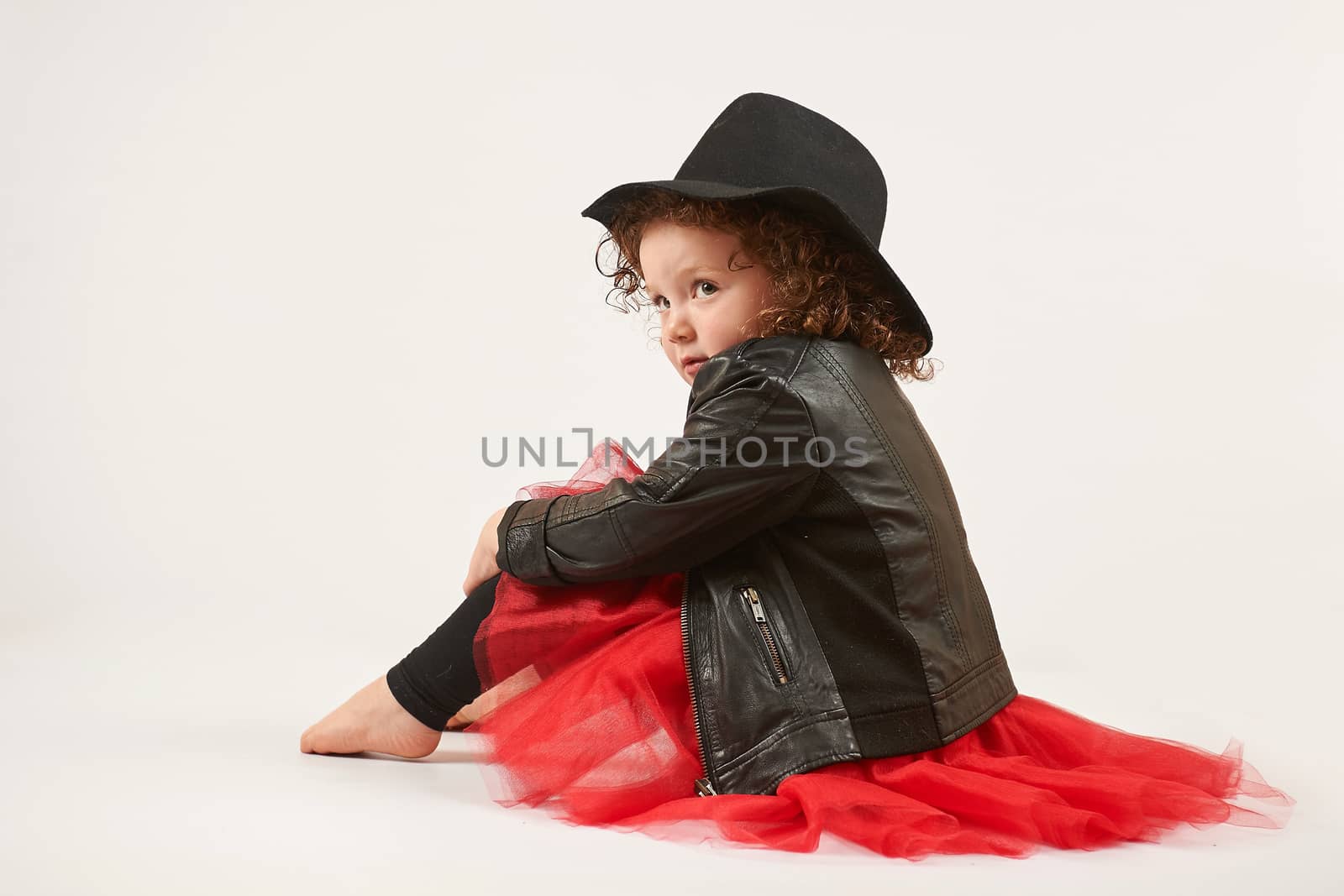 Little girl with black hat sitting and pouting