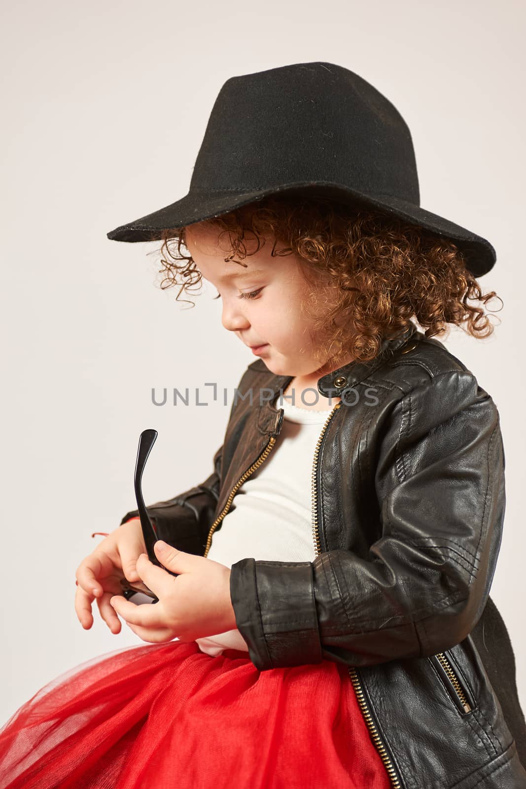 Little girl with black hat sitting looking over sunglasses