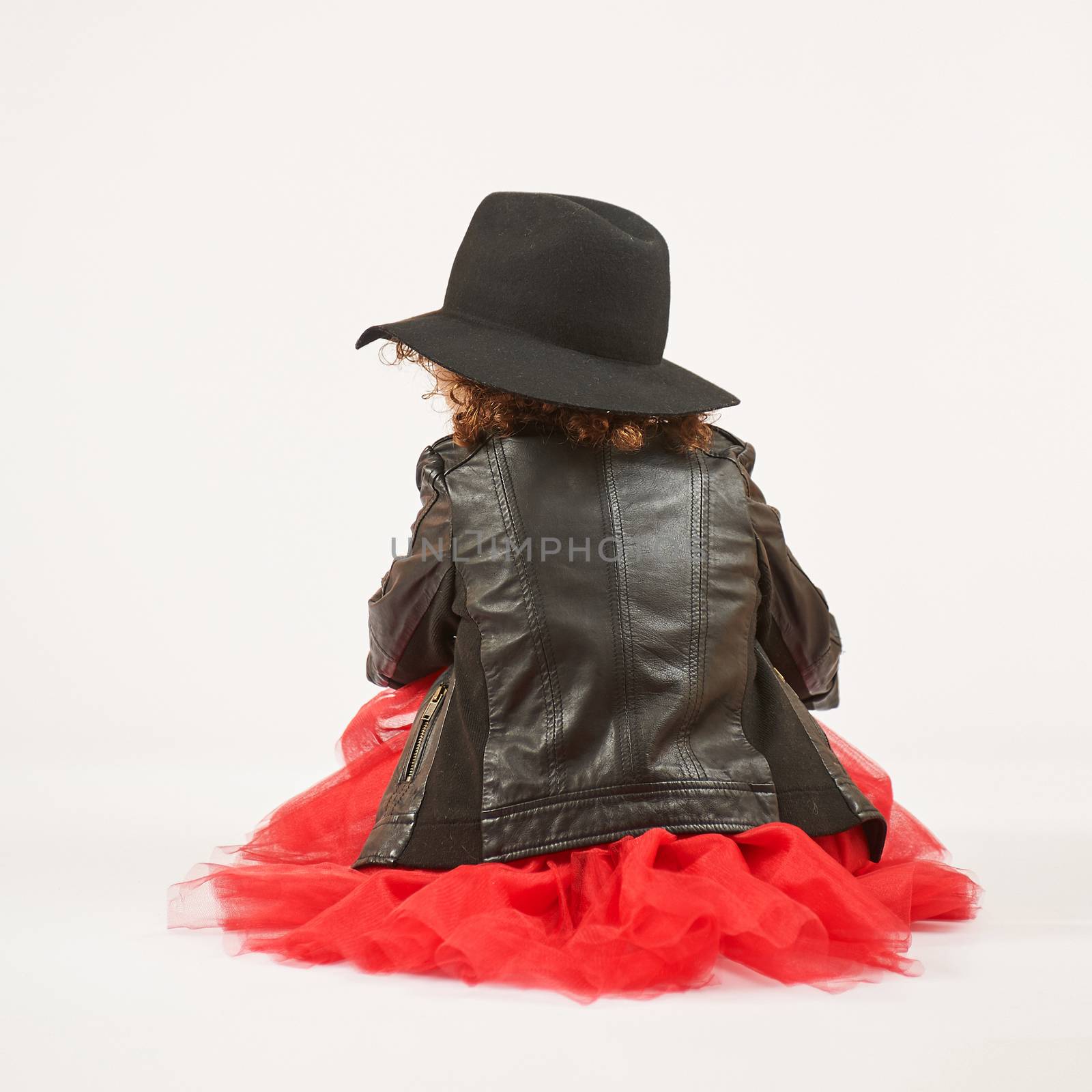 Little girl with black hat sitting and pouting. Back view