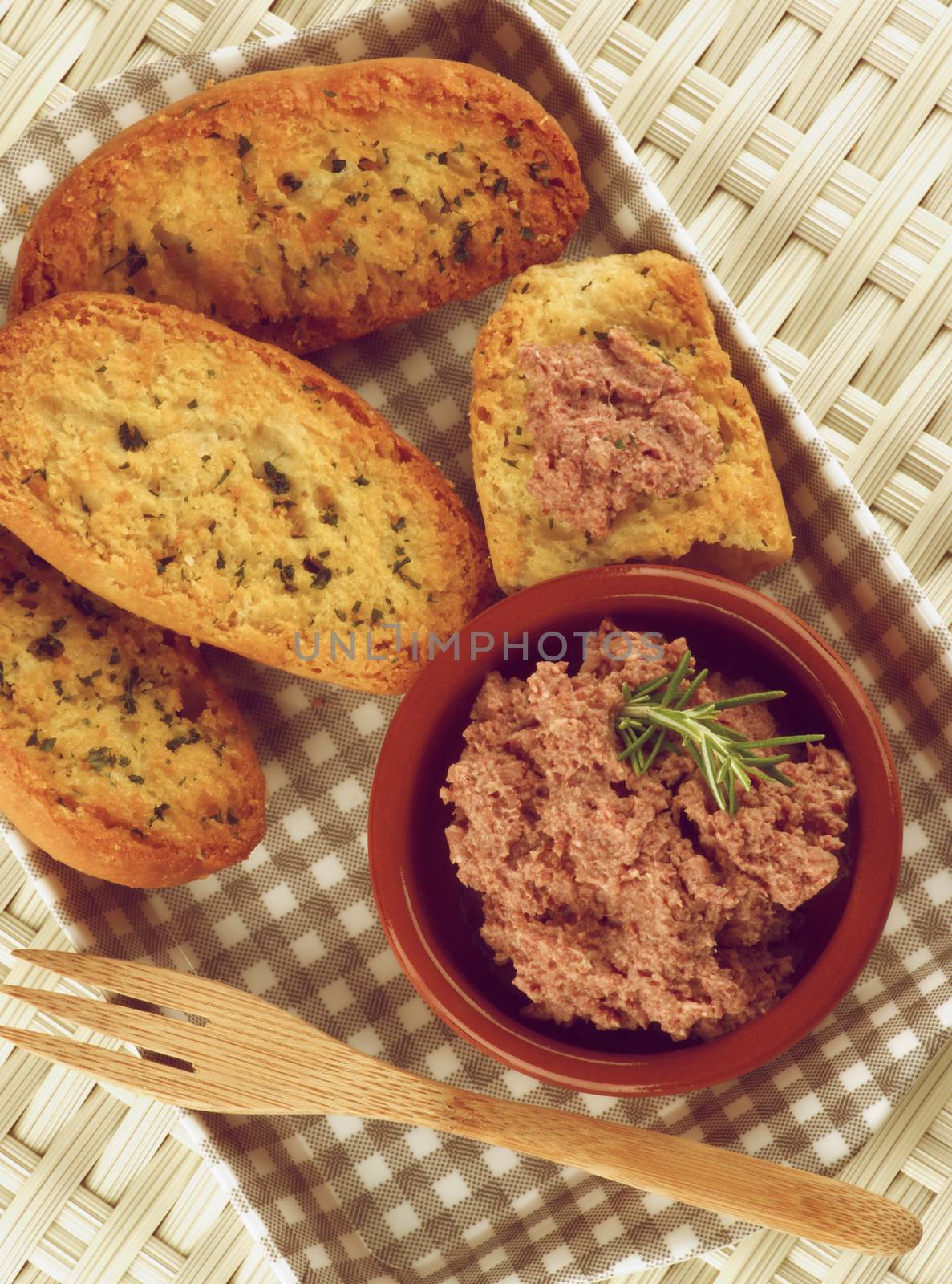 Delicious Homemade Meat Pate with Crispy Herbs Bread in Checkered Tray with Wooden Fork closeup on Wicker background. Retro Styled
