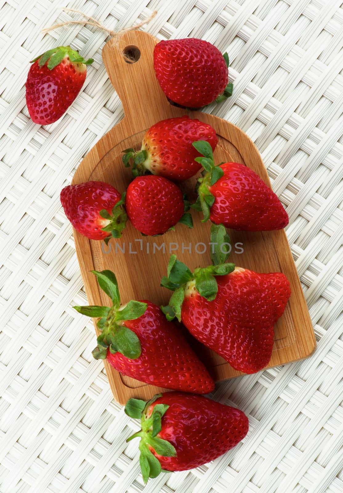 Arrangement of Fresh Ripe Strawberries on Small Wooden Cutting Board closeup on Wicker background. Top View
