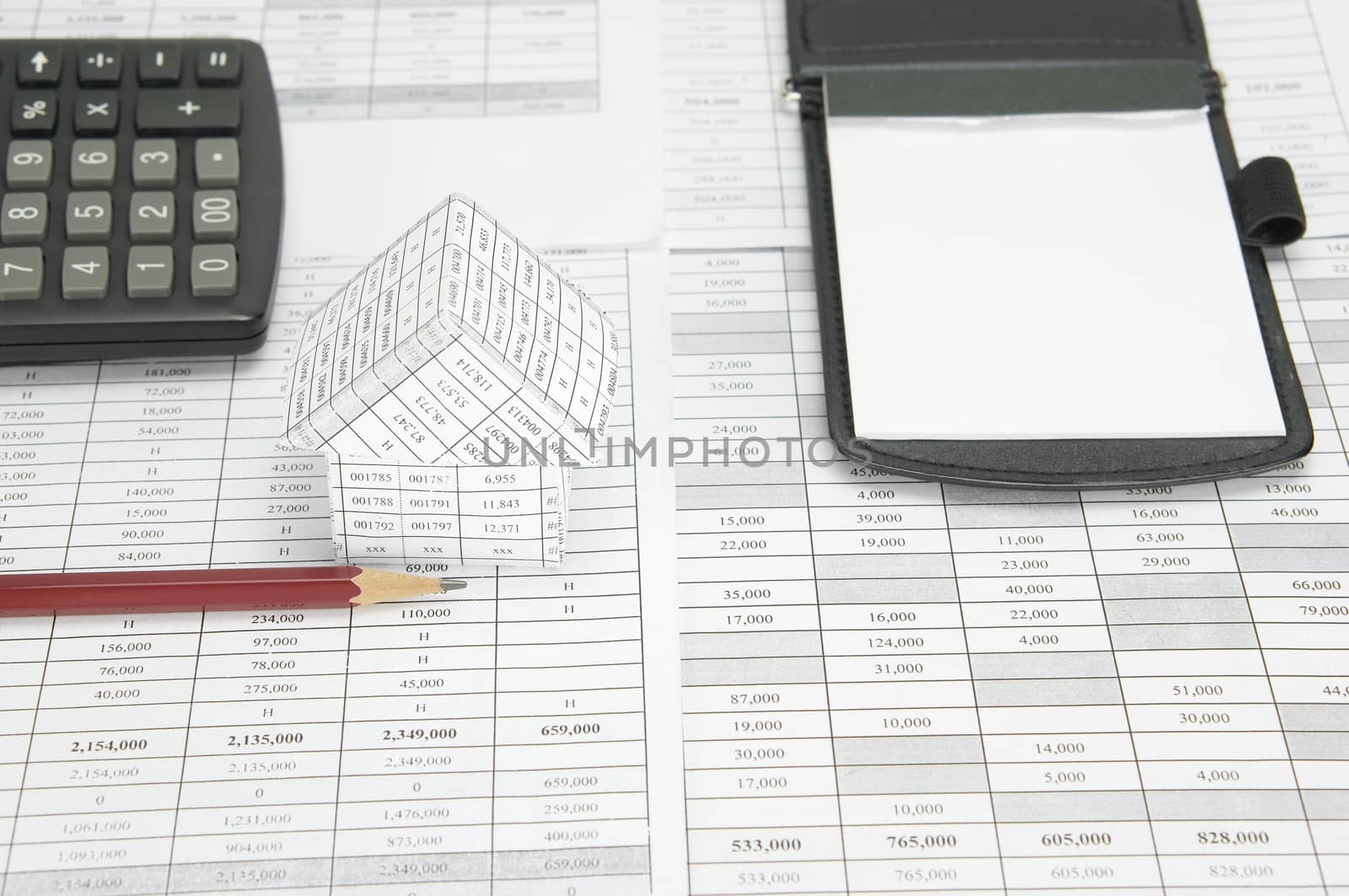 Brown pencil and house on finance account have blur calculator and notepad as background.